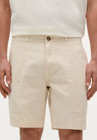 Shorts din bumbac bej, cu buzunare laterale, închidere cu nasture în față și detalii de cusătură vizibile. Design minimalist; croială dreaptă.