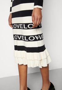 Neulemekko, jossa on mustavalkoisia vaaka-aitoja ja "LOVE"-teksti. Kimalteleva helma lisää tekstuuria. Mallilla on mustat kengät.