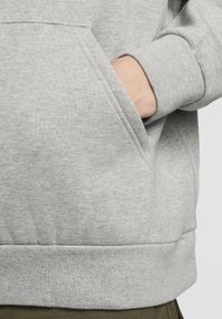 Siv bombažna jopa s kapuco s sprednjim �žepom, rebrastimi manšetami in pasom. Tkanina je mehka na otip z rahlim meliranim vzorcem.