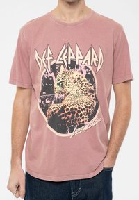 Pink cotton t-shirt featuring a leopard graphic, "Def Leppard" text, and a vintage-style design. Short sleeves and a crew neckline.