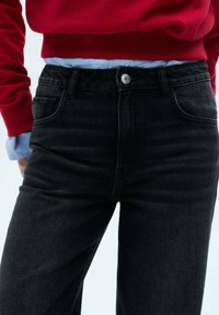 Black denim jeans with a classic straight-leg fit, five-pocket design, and silver button accent, paired with a red sweatshirt and blue shirt.