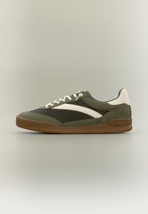 Niski zielony oliwkowy sneaker z białymi akcentami, panelami siateczkowymi, białymi sznurowadłami i brązową gumową podeszwą na neutralnym tle.