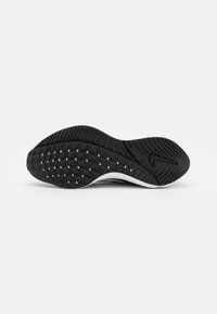 Black athletic shoe outsole with textured rubber pattern and white accents, featuring a raised tread for traction and durability.