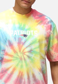 Kortärmad tie-dye t-shirt i pastellfärger av gult, rosa, grönt och blått, med texten "PATRIOTS" och en logotyp i vitt och marinblått.
