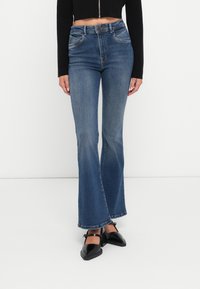Ullendarkeblue jeans med høy midje, lett slitasje og subtile sømdetaljer. Kombinert med svarte sko med firkantet tunge.