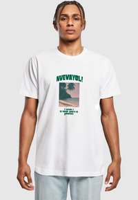 Hvid bomulds-t-shirt med et centralt grafisk motiv af en strandscene med palmer. Teksten lyder "NUEVAYOL!" og "jeg ville ønske, jeg havde taget flere billeder."