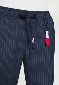 N�ámořnické modré pruhované tepláky s elastickým pasem a šňůrkou, s malou visačkou a očkem na klíče v červené, bílé a modré barvě.