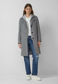 Szary płaszcz z mieszanki wełny o strukturalnym kroju, z jednorzędowym zapięciem i klapami z wycięciami, noszony na białej koszuli i postrzępionych niebieskich dżinsach.