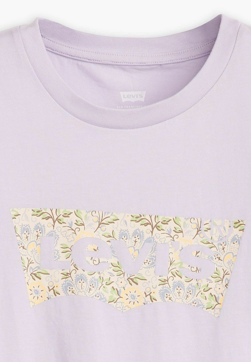 T-shirt di cotone lilla con un grande logo bianco ritagliato, decorato con motivi floreali in verde, blu e giallo. Collo rotondo e maniche corte.