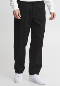 Pantaloni negri din bumbac cu un design drept, dotati cu un fermoar si un nasture. Asortați cu adidași albi pentru un contrast.