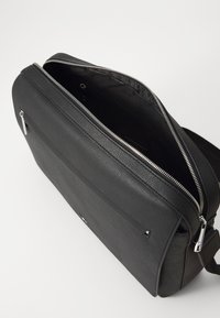 Sac messager en cuir noir avec finition texturée, fermeture zippée et bandoulière réglable. Comprend une poche extérieure et des accents en métal argenté.