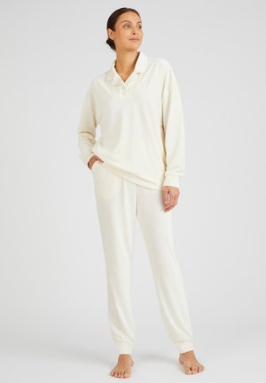 L'ensemble de vêtements d'intérieur crème se compose d'un pull à col avec des boutons et d'un jogging à taille élastique, fabriqué en tissu doux et texturé.