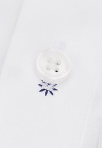 Tkanina białej koszuli z okrągłym, plastikowym guzikiem z czterema otworami oraz niebieską haftowaną gwiazdką w pobliżu guzika. Miękka tekstura, prosty wzór.