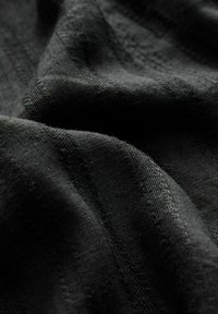 Material negru cu dungi texturate subtile și modele de cusături vizibile, prezentat în falduri moi și vedere de aproape.