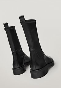 Bottines en cuir noir avec une texture lisse, des panneaux latéraux élastiques et un petit talon large. Elles sont dotées d'une languette à l'arrière pour un enfilage facile.
