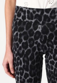 Leggings taille haute avec un motif léopard noir et gris, présentant une texture de tissu lisse et une large ceinture élastique.