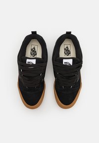 Svarta mockaskor med en brun gummisula, med snörning, vadderad krage och Vans-logotyp på tungan.