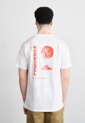White cotton t-shirt featuring a large red graphic on the back, depicting a globe and mountain, with "CONVERSE" text prominently displayed.