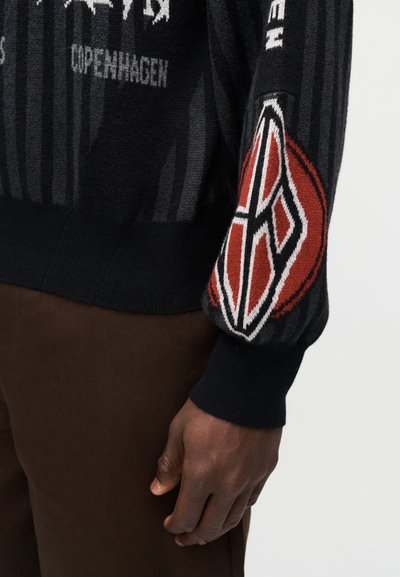 Black knitted sweater featuring striped patterns, red and white accents on the sleeve, and "Copenhagen" text. Soft texture, fitted cuffs.