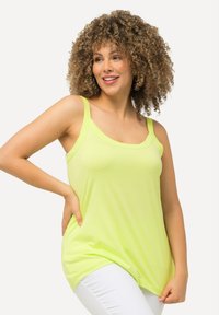 Limonengrünes Tanktop mit breiten Trägern, entspannter Passform und Rundhalsausschnitt, kombiniert mit weißen Hosen. Weicher, glatter Stoff.
