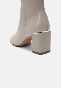 Bottine en cuir beige avec un talon bloc et une bordure métallique près du bord supérieur.
