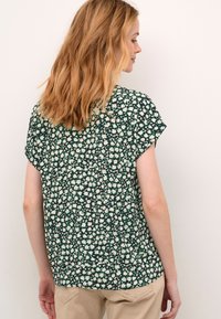 Camicia a stampa floreale in verde scuro, con maniche corte, un tessuto leggero e una vestibilità rilassata, decorata con piccoli fiori bianchi e rosa.