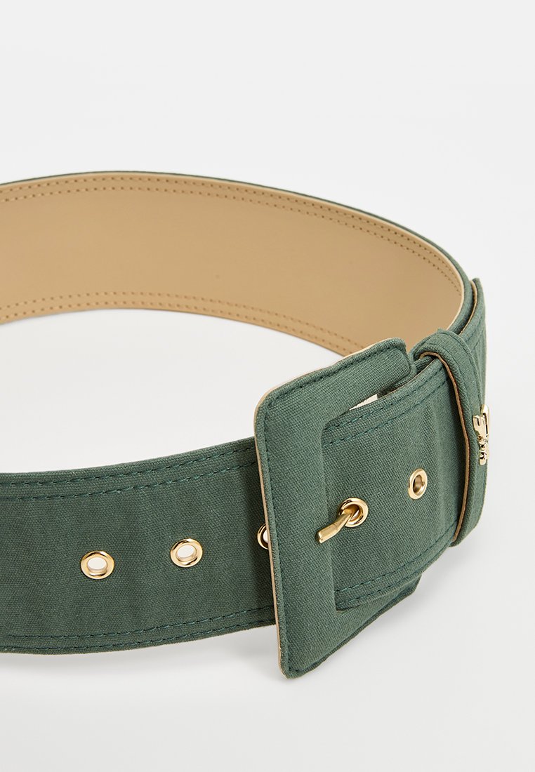 Grüner Stoffgurt mit breitem Design, ausgestattet mit einer goldenen Metall-Buckle, Ösen und Nähdetails an den Kanten. Die Innenseite ist beige.