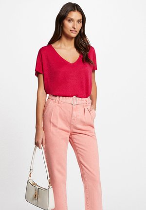 Top rouge à manches courtes en V, associé à un pantalon taille haute rose clair et un petit sac à main blanc avec des accents noirs.