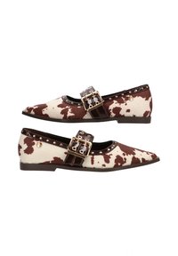 Zapatos planos puntiagudos hechos de tela de color blanco roto con estampado de vaca marrón. Presentan una correa de cuero marrón con hebilla dorada y acentos de tachuelas.