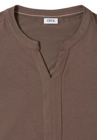 Brązowa bluzka z krótkim rękawem, z dekoltem w serek, subtelną fakturą oraz metką "CECIL" na wewnętrznym kołnierzu.