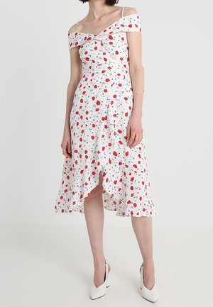 Woman wearing white off-shoulder midi dress with red and blue floral print and ruffled hem, paired with white pointed-toe heels.