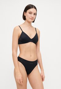 Schwarzes Bikini-Set mit einem minimalistischen, dreieckigen Bralette und niedrigen, nahtlosen Unterteilen, gefertigt aus glattem Stoff mit dezentem Branding.
