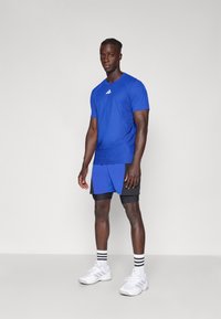 Camiseta atlética azul con patrón texturizado, combinada con pantalones cortos azules y negros. Calzado blanco con calcetas de rayas negras en contraste.