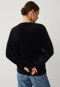 Zwarte, zachte trui met lange mouwen, voorzien van een comfortabele pasvorm en ronde hals. De textuur lijkt zacht en fluweelachtig tegen een blauwe spijkerbroek.