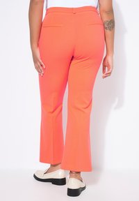 Koraalroze uitlopende broek van een gladde stof met achterzakken. Draagt wit loafers met een getextureerde zool en lage hak.