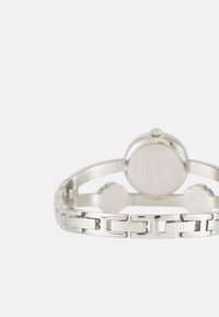 Silver stainless steel watch with a linked band, round face, and embossed brand logo. Smooth texture with polished and matte finishes.