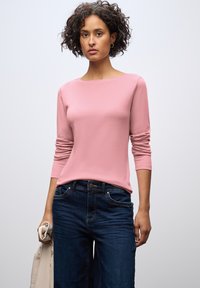 Lichtroze langemouwen top met een ronde halslijn, gecombineerd met donkerblauwe jeans. Glad materiaal, getailleerd ontwerp en zichtbare stiksels.