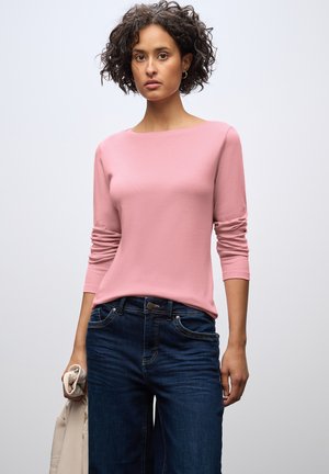 Lichtroze langemouwen top met een ronde halslijn, gecombineerd met donkerblauwe jeans. Glad materiaal, getailleerd ontwerp en zichtbare stiksels.
