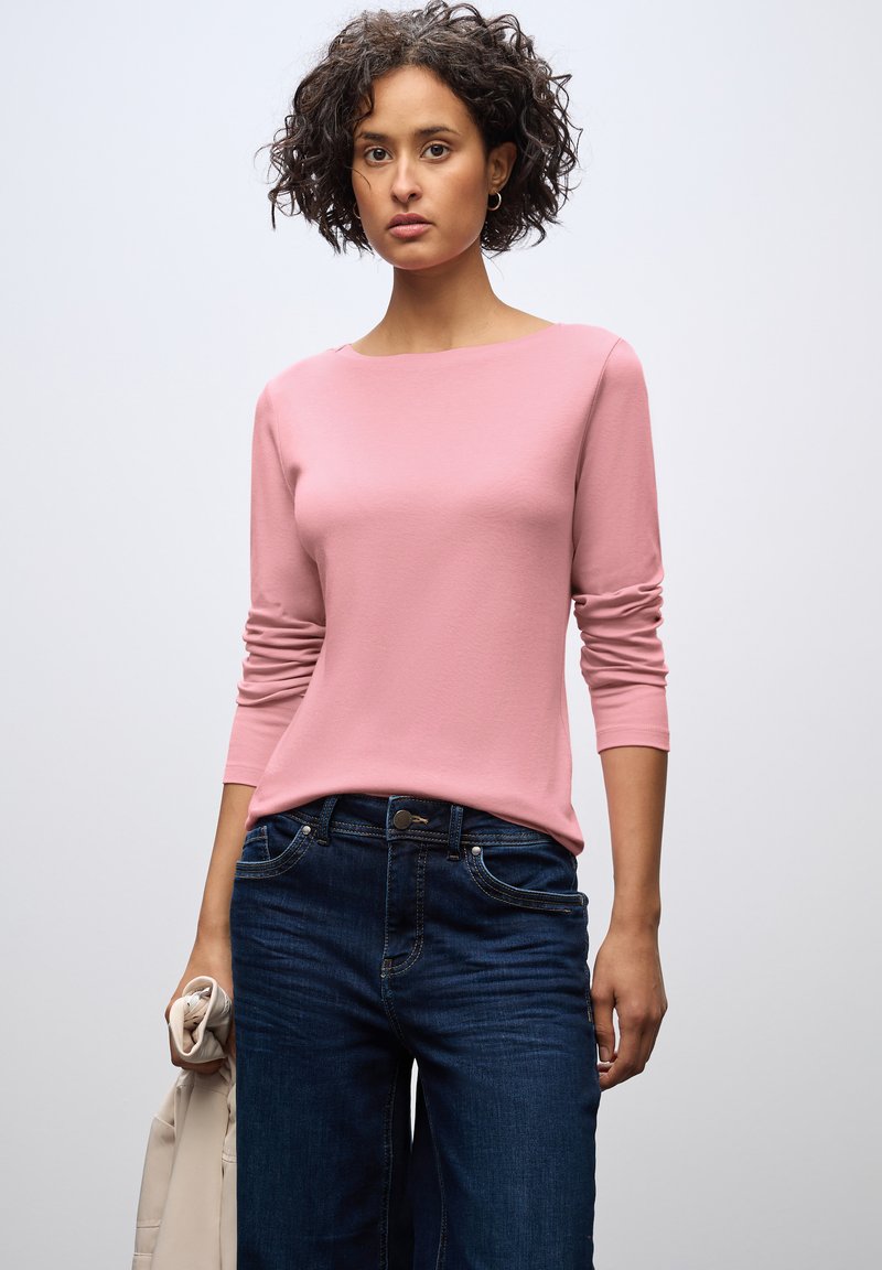 Lichtroze langemouwen top met een ronde halslijn, gecombineerd met donkerblauwe jeans. Glad materiaal, getailleerd ontwerp en zichtbare stiksels.