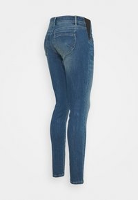 Skinny jeans in dark blue denim with a faded finish. Features a traditional five-pocket design and black panel accents at the waist.