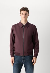 Burgundy tõmblukuga jakk klassikalise kraega, soonikuvarrukatega ja elastse allääriga; valmistatud siledast, kergest kangast; sobitatud tumedate teksadega.