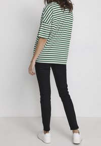 Camiseta a rayas verde y blanca de manga corta, combinada con jeans skiny negros y zapatillas blancas, vista desde la parte posterior.