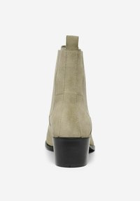 Botín de ante beige con un acabado suave, un tacón bajo apilado y detalles de costura sutiles, que cuenta con una pestaña en la parte posterior.