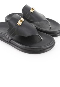 Las chanclas de cuero negro presentan un diseño con separador para el dedo, una correa de cuero con forma curvada y un acento de hebilla en tono dorado. Suela texturizada.