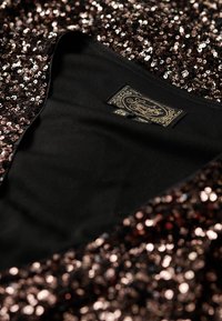 Tissu noir orné de sequins bronze, créant un effet scintillant. L'intérieur est noir uni, avec une étiquette de marque.