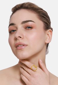 Bague en métal doré présentant un design twisted et organique. Portée au doigt, mettant en valeur sa forme sculpturale et sa texture lisse.