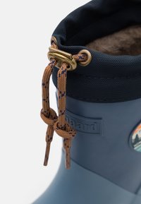Botte en caoutchouc bleue avec une tige en nylon texturée bleu marine, fermeture à cordon de serrage et quincaillerie de couleur bronze. Présente un patch avec un logo rond au design de montagne.