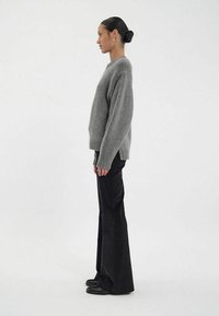 Pull gris en maille avec une coupe décontractée, poignets côtelés, assorti à un pantalon noir évasé et des chaussures noires. Vue de côté.