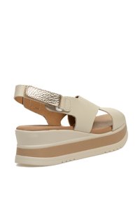 Sandalia de tacón en piel beige con un acento metálico dorado, suela tipo plataforma, punta abierta y plantilla texturizada. Cuenta con correa para el talón ajustable.