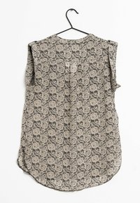 Blusa a maniche corte su una gruccia nera, realizzata in tessuto beige con un motivo floreale e paisley nero, orlo arrotondato e vestibilità ampia.